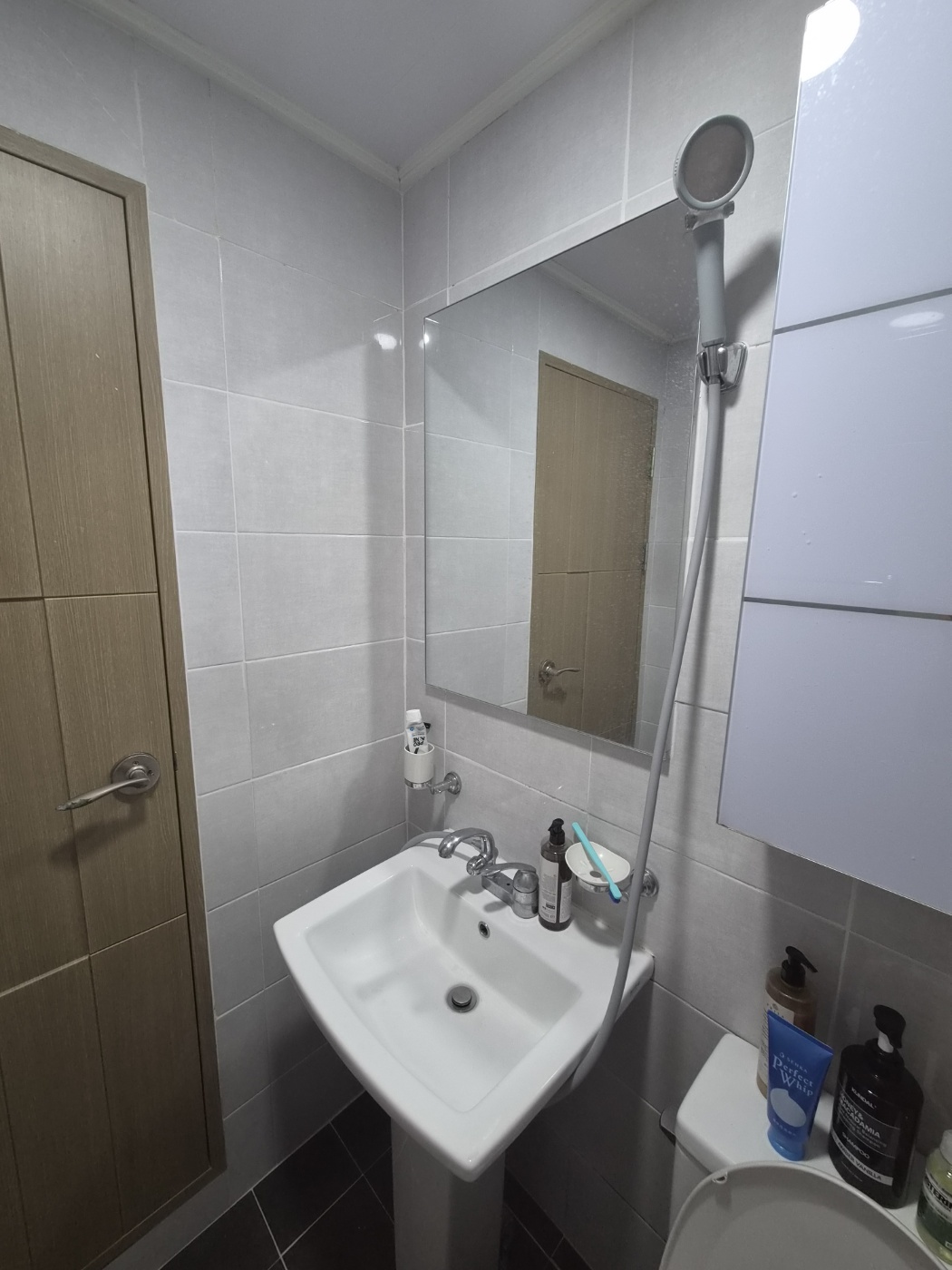 The shower holder above the sink, on the wall opposite the towel bar